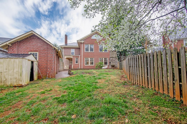 rear view of house featuring a chimney, an outbuilding, brick siding, a fenced backyard, and a yard