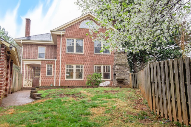 rear view of property featuring a chimney, a fenced backyard, brick siding, and a yard