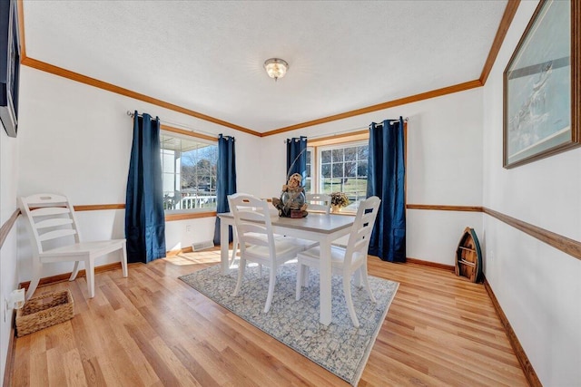 dining area featuring light wood-style floors, crown molding, a healthy amount of sunlight, and baseboards