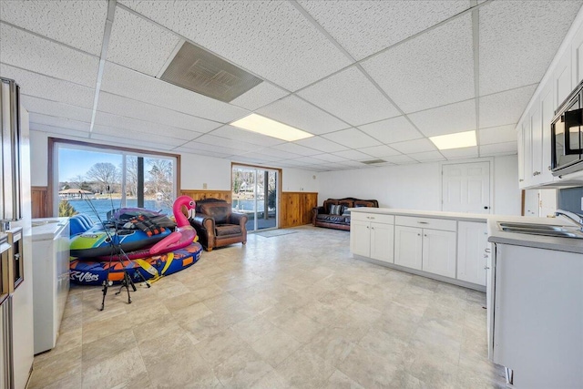 interior space with visible vents, light floors, a sink, a paneled ceiling, and wainscoting
