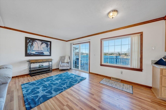 living room featuring baseboards, visible vents, crown molding, and light wood finished floors