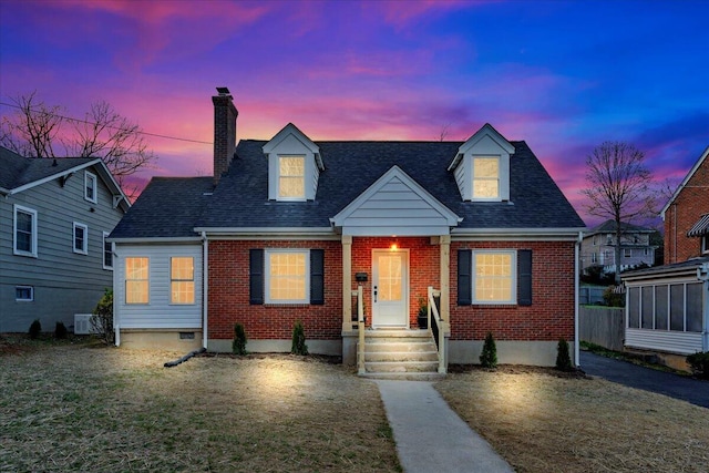 new england style home with a shingled roof, a chimney, brick siding, and a front yard