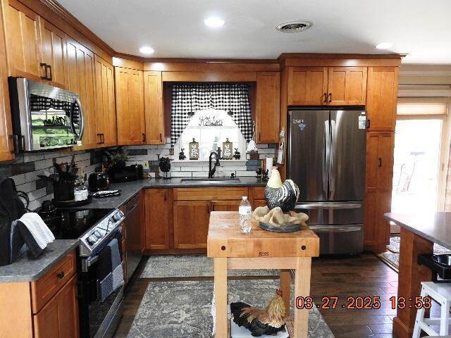 kitchen with stainless steel appliances, a sink, dark wood-style flooring, dark countertops, and brown cabinets