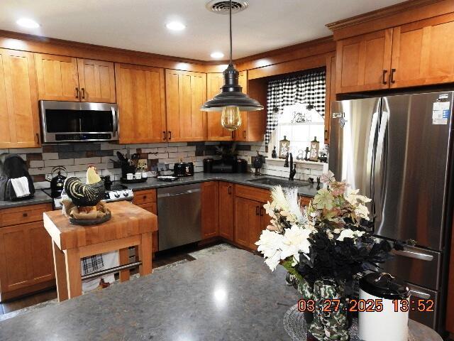 kitchen featuring stainless steel appliances, backsplash, dark countertops, a sink, and brown cabinetry