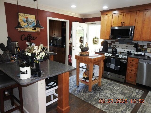 kitchen featuring brown cabinets, stainless steel appliances, backsplash, ornamental molding, and dark wood-type flooring