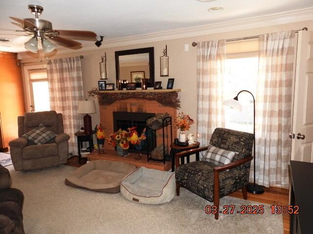 living area with a brick fireplace, crown molding, and ceiling fan