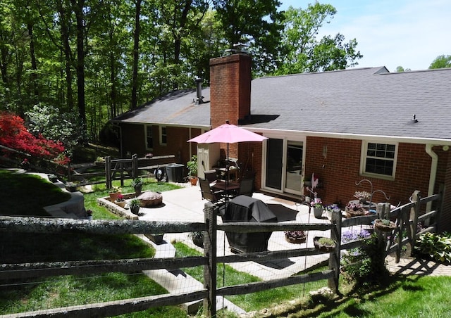 rear view of property featuring roof with shingles, a chimney, brick siding, fence private yard, and a patio