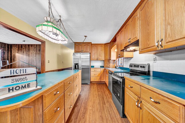 kitchen featuring a textured ceiling, light wood finished floors, appliances with stainless steel finishes, under cabinet range hood, and a sink