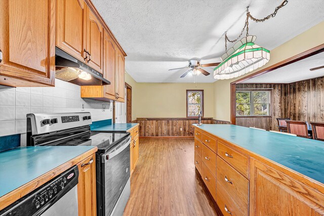 kitchen with a wainscoted wall, a textured ceiling, light wood finished floors, stainless steel appliances, and under cabinet range hood