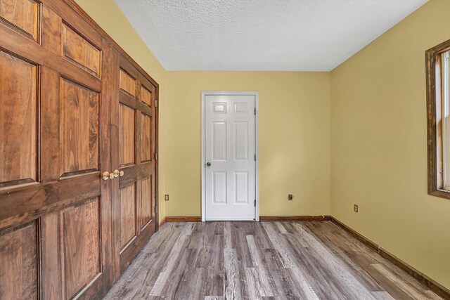 unfurnished bedroom featuring baseboards, a textured ceiling, and wood finished floors