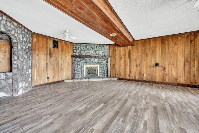 unfurnished living room featuring a textured ceiling, beamed ceiling, a fireplace, wood finished floors, and a ceiling fan