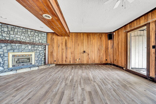 unfurnished living room featuring a textured ceiling, wooden walls, visible vents, ceiling fan, and wood finished floors