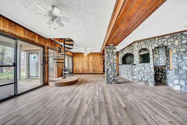 unfurnished living room featuring a ceiling fan, a textured ceiling, wooden walls, and wood finished floors