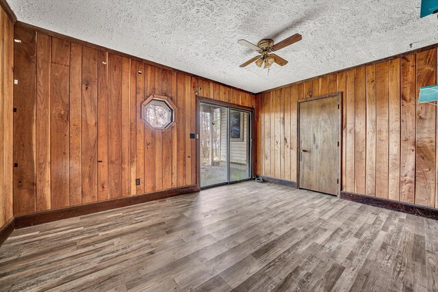 unfurnished room featuring wooden walls, wood finished floors, a textured ceiling, baseboards, and ceiling fan