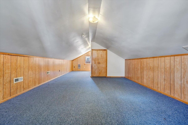 additional living space with visible vents, wood walls, baseboards, and vaulted ceiling
