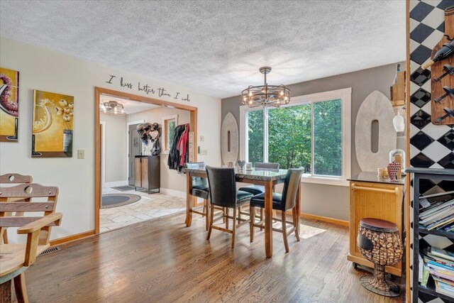 dining space with baseboards, light wood-style flooring, a textured ceiling, and a chandelier