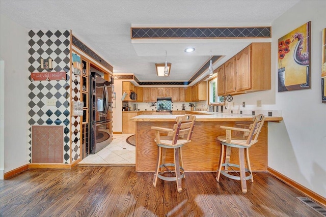 kitchen with freestanding refrigerator, light wood-style flooring, a peninsula, and light countertops