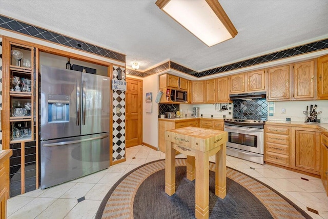 kitchen with under cabinet range hood, light tile patterned flooring, a textured ceiling, and appliances with stainless steel finishes