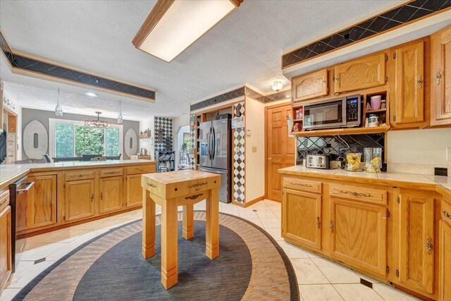 kitchen featuring stainless steel appliances, a textured ceiling, a notable chandelier, and light tile patterned floors