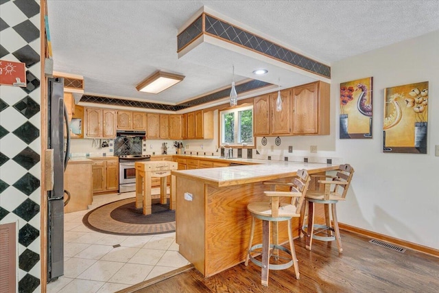 kitchen with a textured ceiling, stainless steel appliances, a peninsula, under cabinet range hood, and visible vents