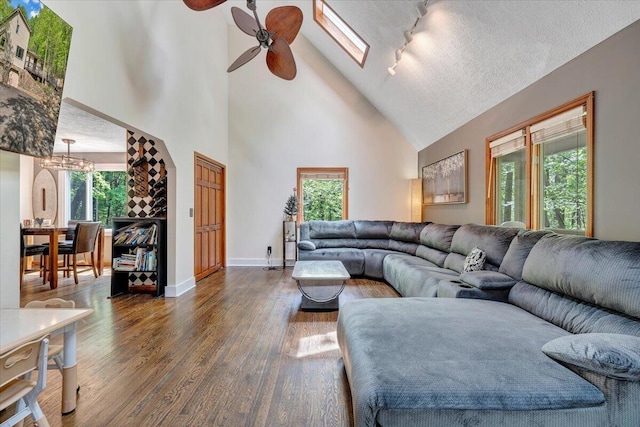 living area featuring high vaulted ceiling, baseboards, ceiling fan with notable chandelier, and dark wood finished floors