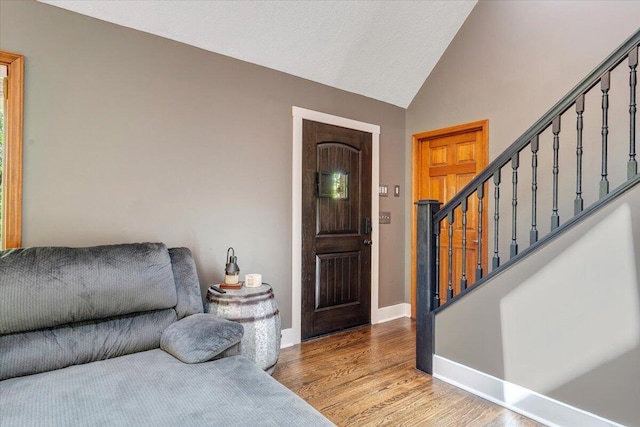 entrance foyer with baseboards, vaulted ceiling, wood finished floors, and stairway