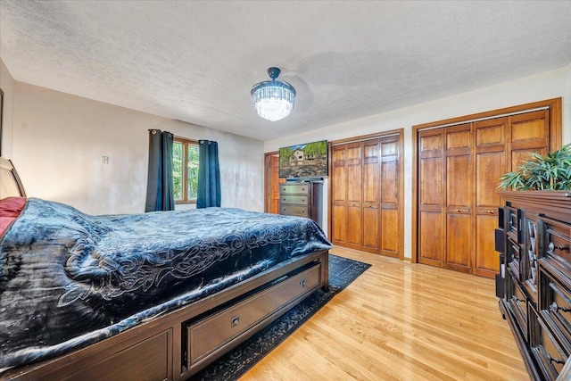 bedroom with multiple closets, a textured ceiling, a notable chandelier, and light wood-type flooring