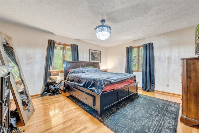 bedroom featuring light wood-style floors, baseboards, an inviting chandelier, and a textured ceiling