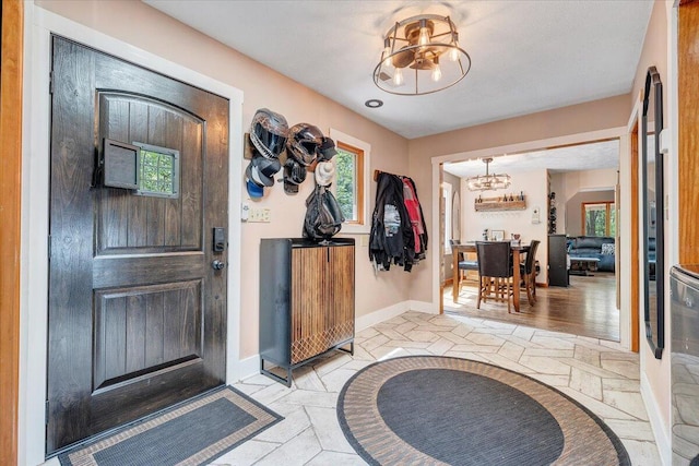 entryway featuring stone tile flooring, baseboards, a chandelier, and a wealth of natural light