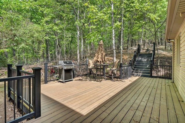 wooden terrace featuring stairs, a grill, outdoor dining space, and a forest view