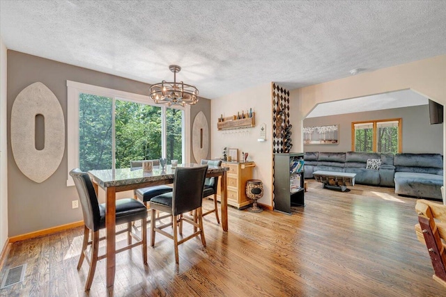 dining room featuring a textured ceiling, visible vents, wood finished floors, baseboards, and a notable chandelier