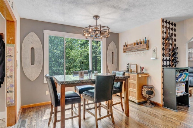 dining area featuring light wood-style floors, visible vents, a textured ceiling, and a notable chandelier