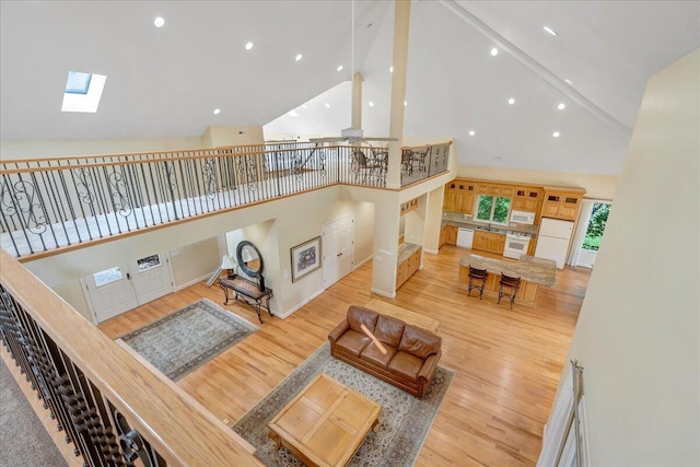 living area featuring high vaulted ceiling, wood finished floors, a skylight, and recessed lighting