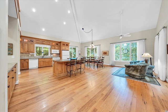 kitchen featuring a wealth of natural light, white appliances, light wood-type flooring, a breakfast bar area, and a center island
