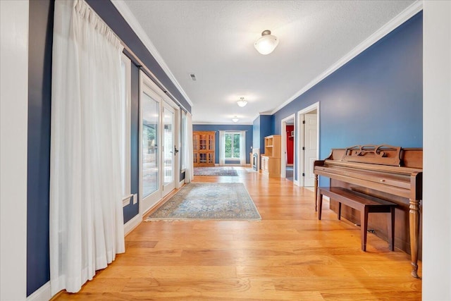 hall with visible vents, baseboards, ornamental molding, light wood-type flooring, and french doors