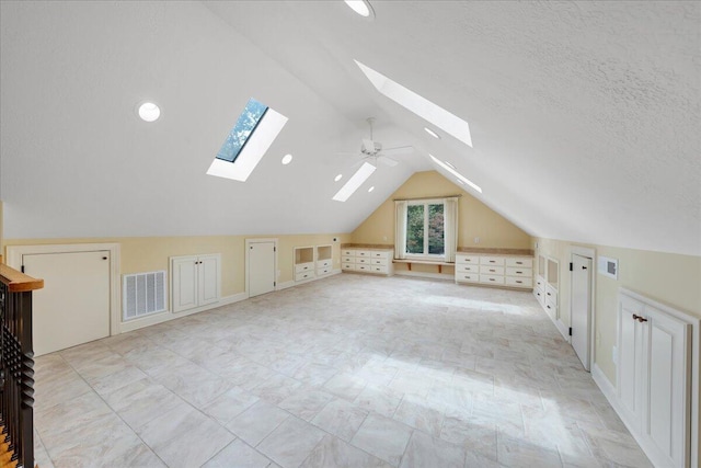bonus room with built in features, a textured ceiling, visible vents, and vaulted ceiling with skylight