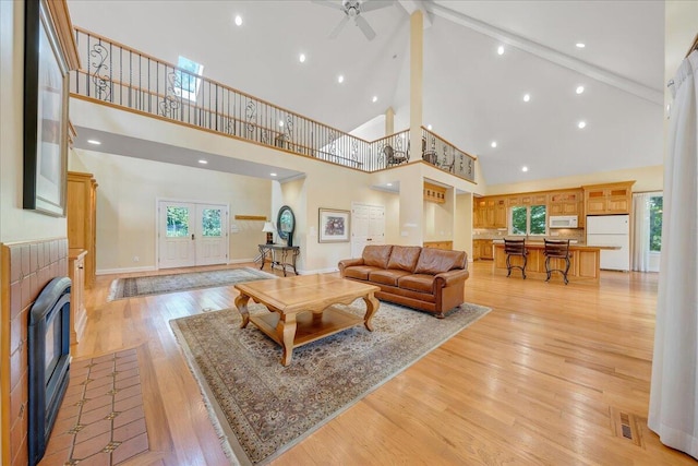 living room featuring high vaulted ceiling, a tile fireplace, baseboards, a ceiling fan, and light wood-style floors
