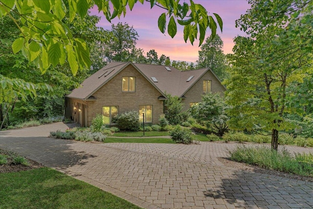 view of front of home with an attached garage, brick siding, a shingled roof, a lawn, and decorative driveway