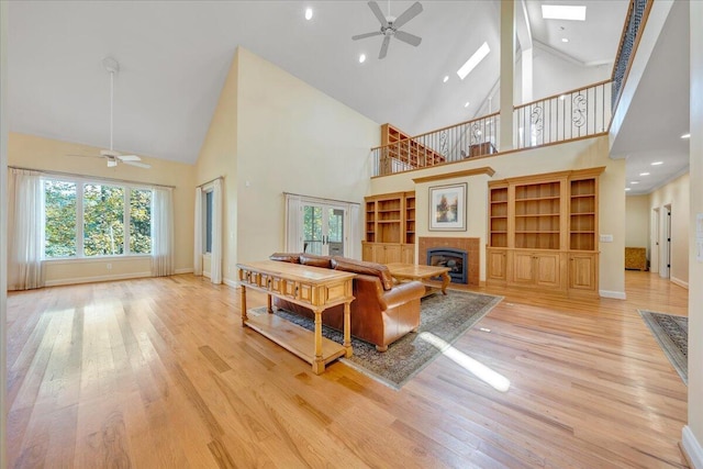 living room with baseboards, light wood-style flooring, a tile fireplace, and a ceiling fan