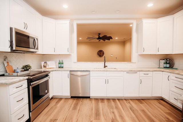 kitchen with white cabinets, light stone countertops, appliances with stainless steel finishes, a sink, and light wood-type flooring