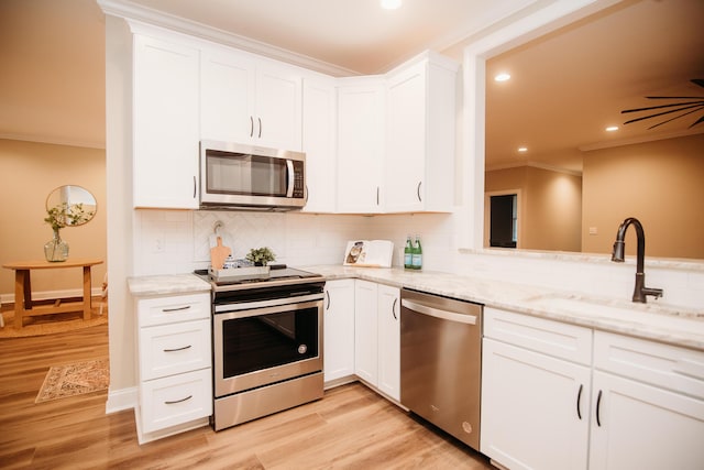 kitchen featuring ornamental molding, backsplash, a sink, light wood finished floors, and appliances with stainless steel finishes