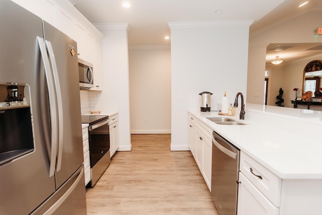 kitchen featuring a sink, light wood finished floors, appliances with stainless steel finishes, a peninsula, and ornamental molding