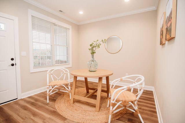 dining space featuring baseboards, visible vents, wood finished floors, and crown molding