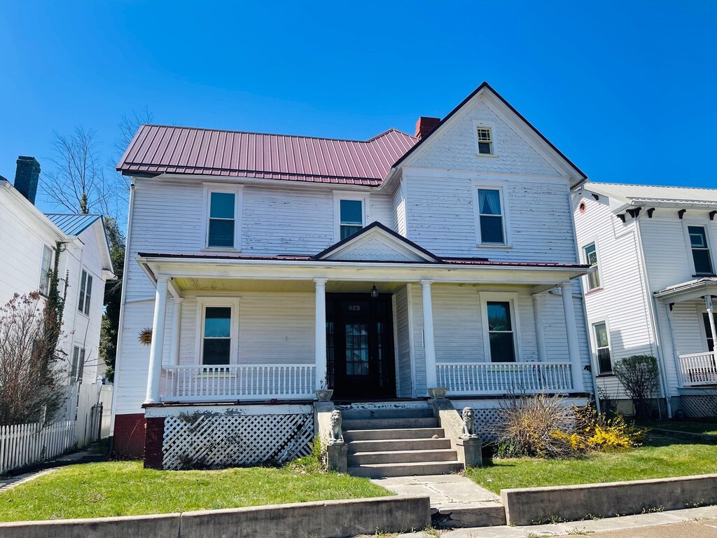 view of front of home with a porch, a standing seam roof, fence, and metal roof