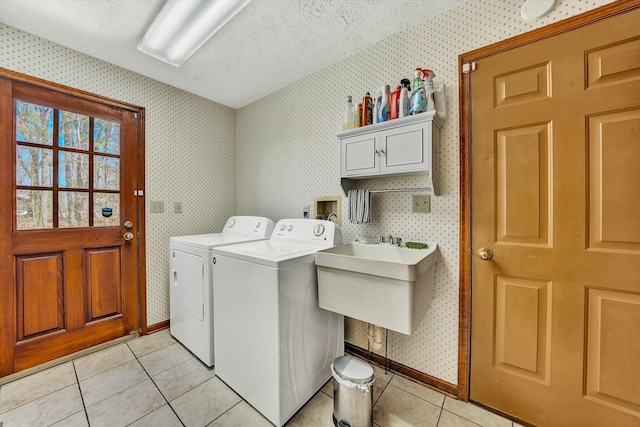 washroom with a textured ceiling, wallpapered walls, a sink, washer and dryer, and cabinet space