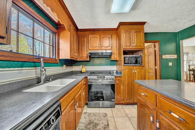kitchen with a sink, appliances with stainless steel finishes, dark countertops, under cabinet range hood, and wallpapered walls