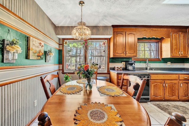 dining room with light tile patterned flooring, a textured ceiling, wainscoting, wallpapered walls, and an inviting chandelier