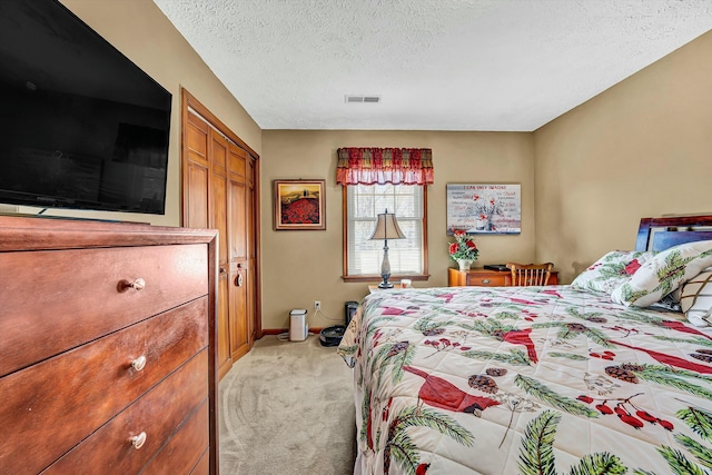 bedroom with a closet, light carpet, a textured ceiling, baseboards, and visible vents