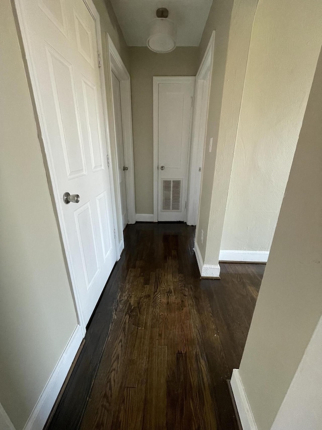 corridor featuring dark wood finished floors, baseboards, and visible vents