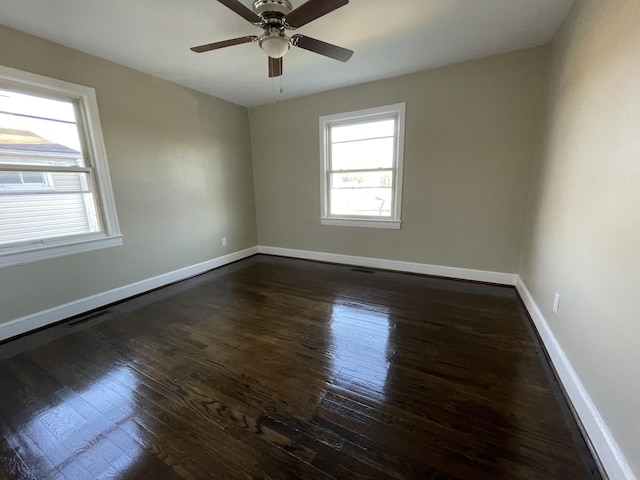 empty room featuring dark wood-type flooring, visible vents, baseboards, and a ceiling fan